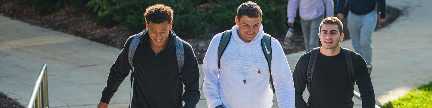 Three male students walking on campus near the Hawthorn Building